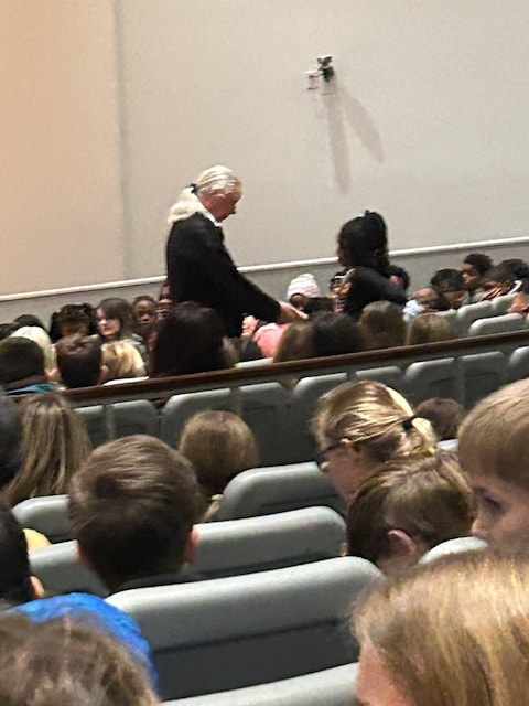 "Speaker addressing a seated audience in a lecture hall, viewed from the back of the room."