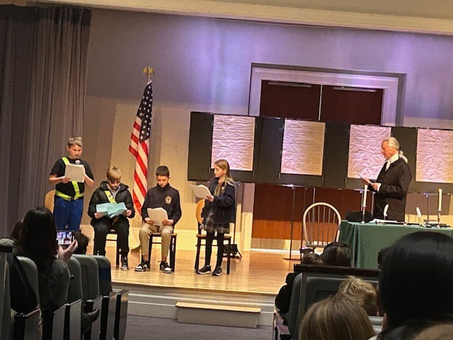 "Panel discussion on a stage with multiple seated speakers, American flag displayed beside the stage."