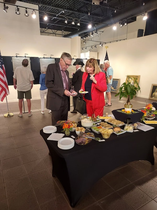 "Attendees gathered around a refreshment table during a reception in a gallery space."